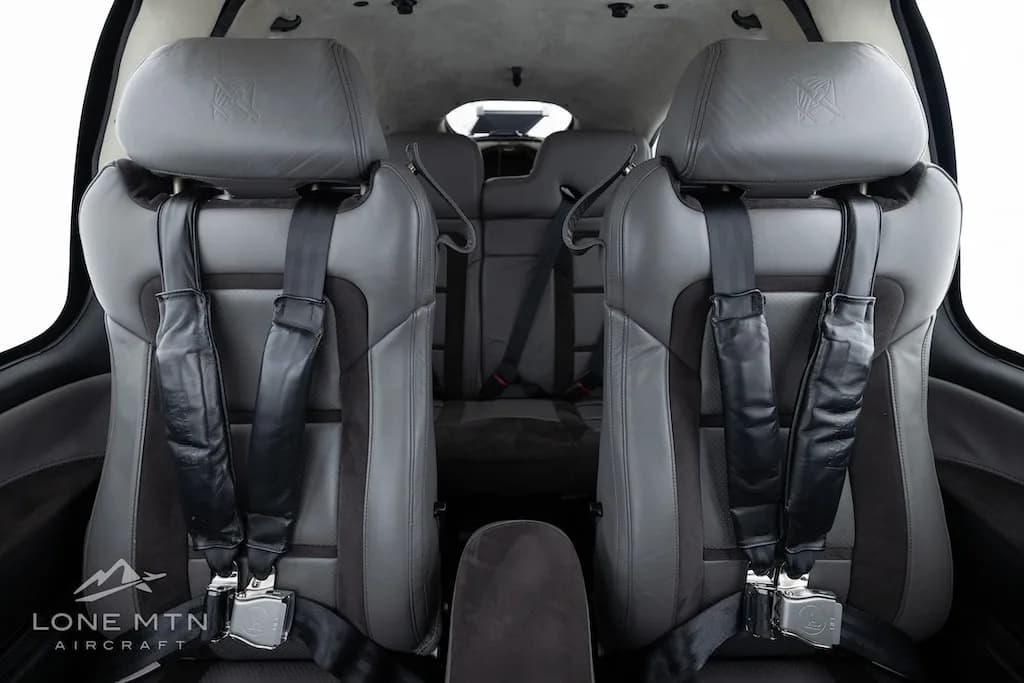 The gray and dark gray front cabin seats of an aircraft, viewed from the rear, with seatbelts visible.