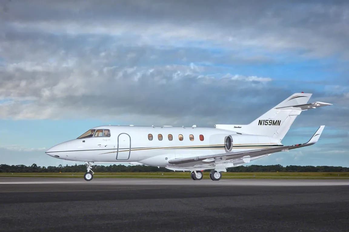 A white business jet with gold and black stripes, tail number N159MN, seen from the side on a tarmac.