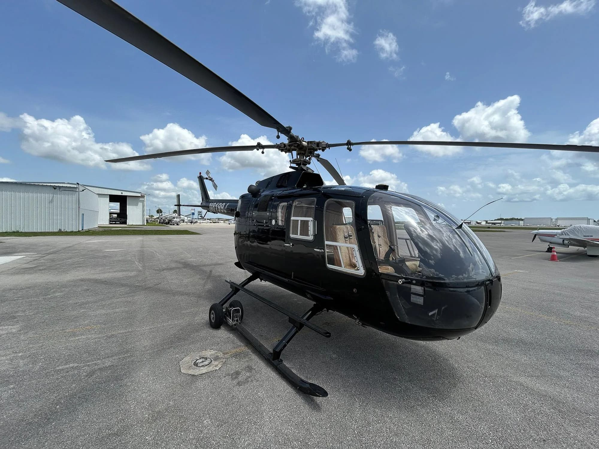 A black helicopter sits on the tarmac under a partly cloudy sky.