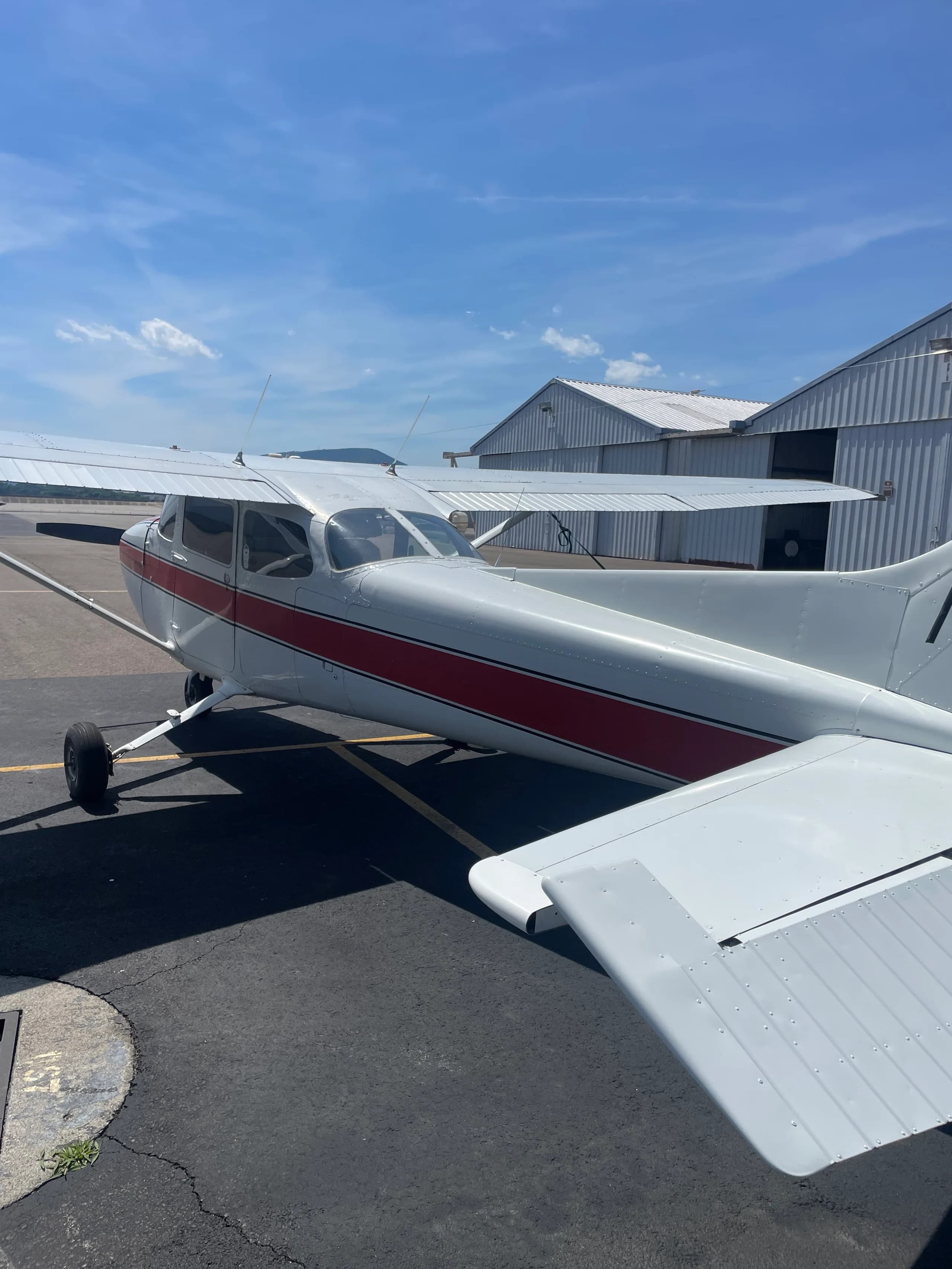 A rear-side view of the white and red Cessna 172, registration N733EN, parked near hangars.