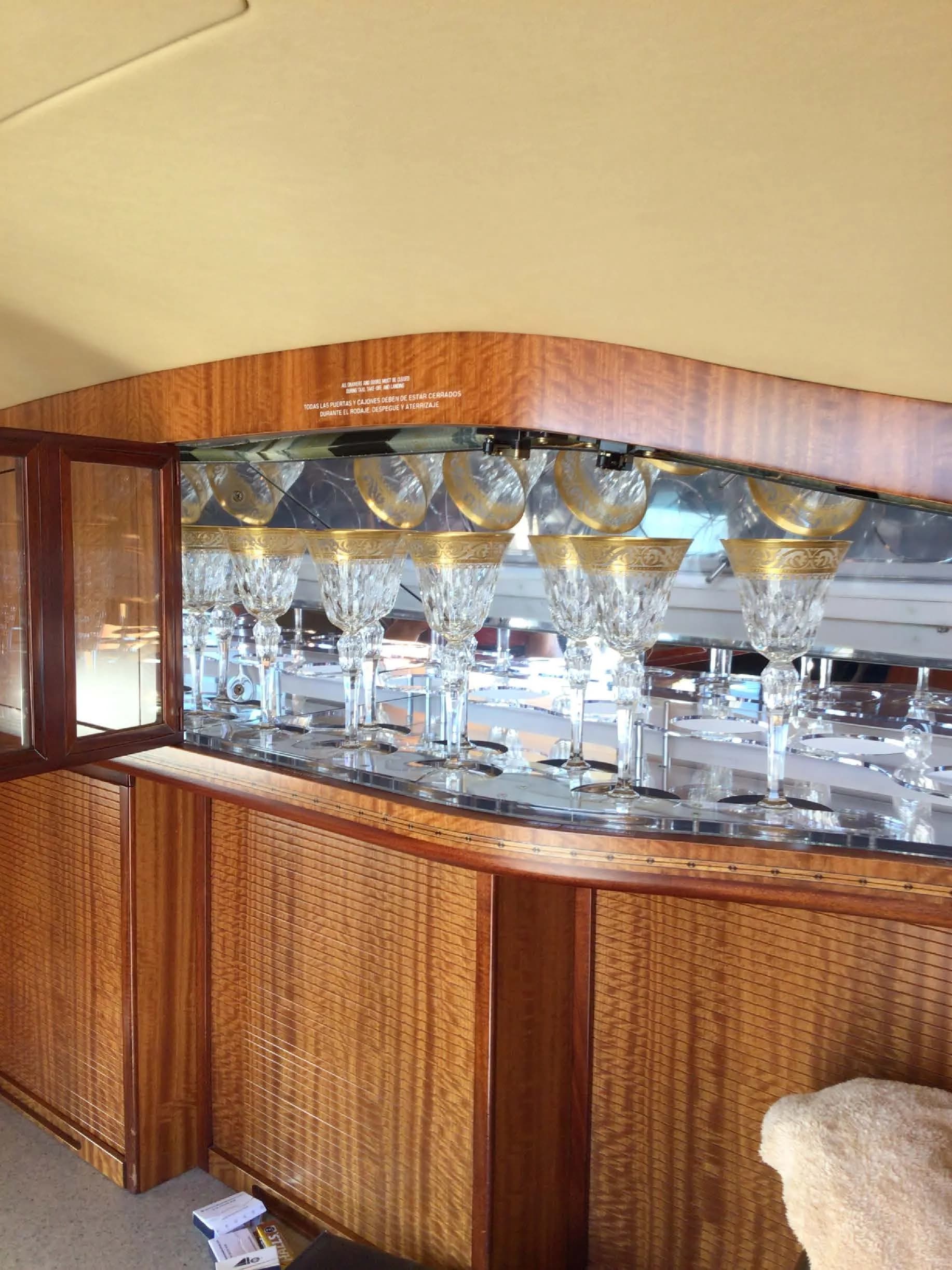 An open cabinet inside an aircraft, revealing a display of ornate crystal glasses with gold rims.