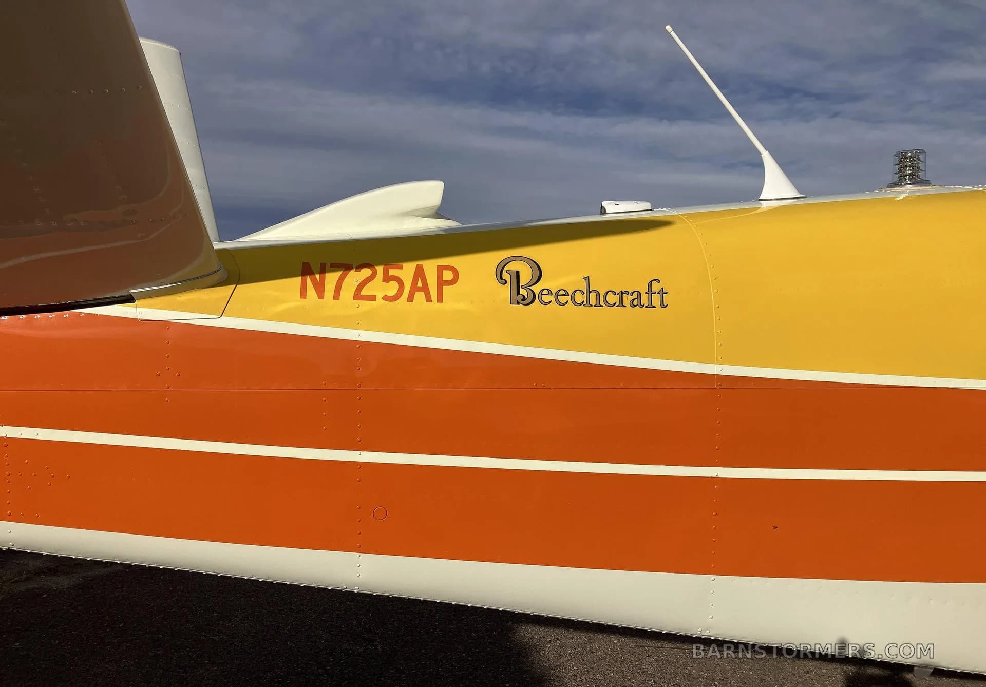A close-up of the tail section of a white, orange, and yellow Beechcraft Bonanza N725AP, showing the N-number and "Beechcraft" logo.