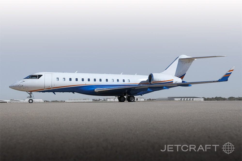 A white and blue business jet with orange stripes parked on a tarmac under a clear sky.