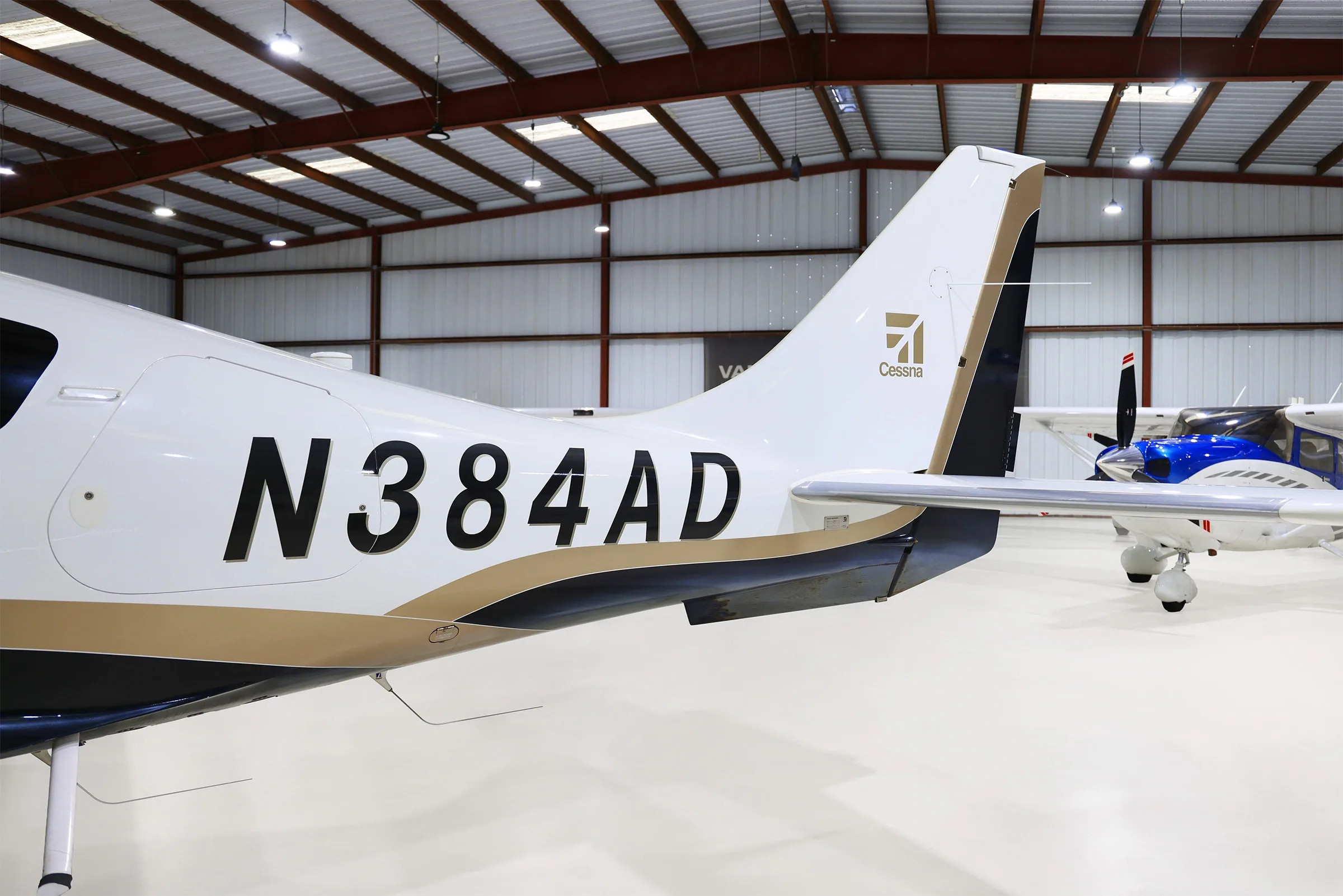 A close-up view of the tail of the white, black, and gold Cessna TTx aircraft (N384AD) in a hangar.