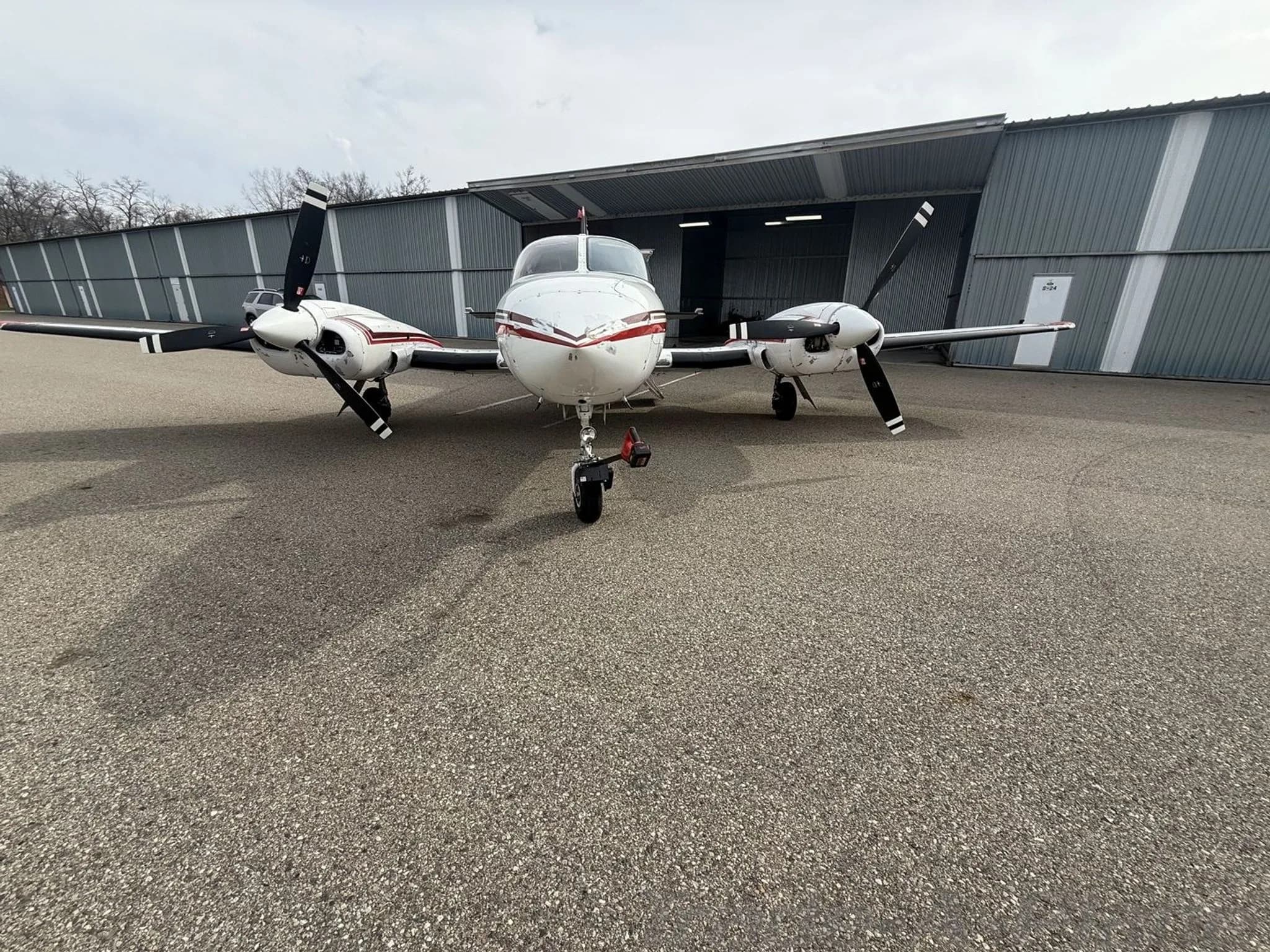 A front view of a white and red twin-engine Cessna 414 Chancellor aircraft, registration N4492U, parked on an asphalt ramp in front of a hangar.