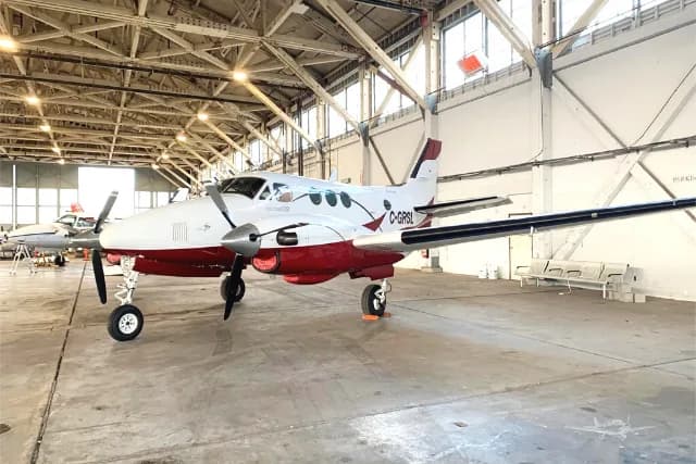 A white and red twin-engine turboprop aircraft, likely a Beechcraft King Air, with registration C-GRSL, parked inside a large hangar.