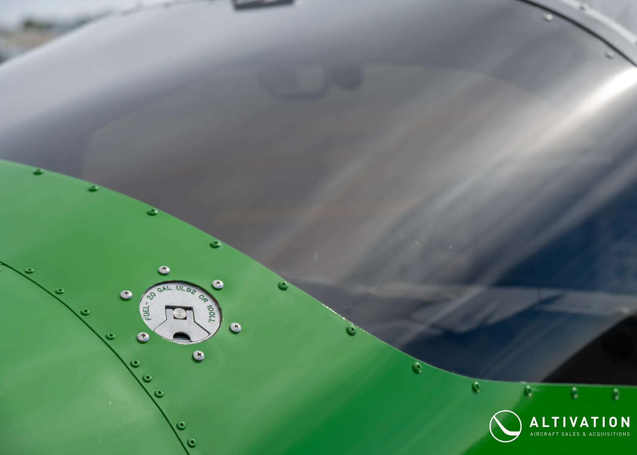 A close-up of the green fuselage and fuel cap of a Vans RV-12 aircraft, showing fuel type markings.