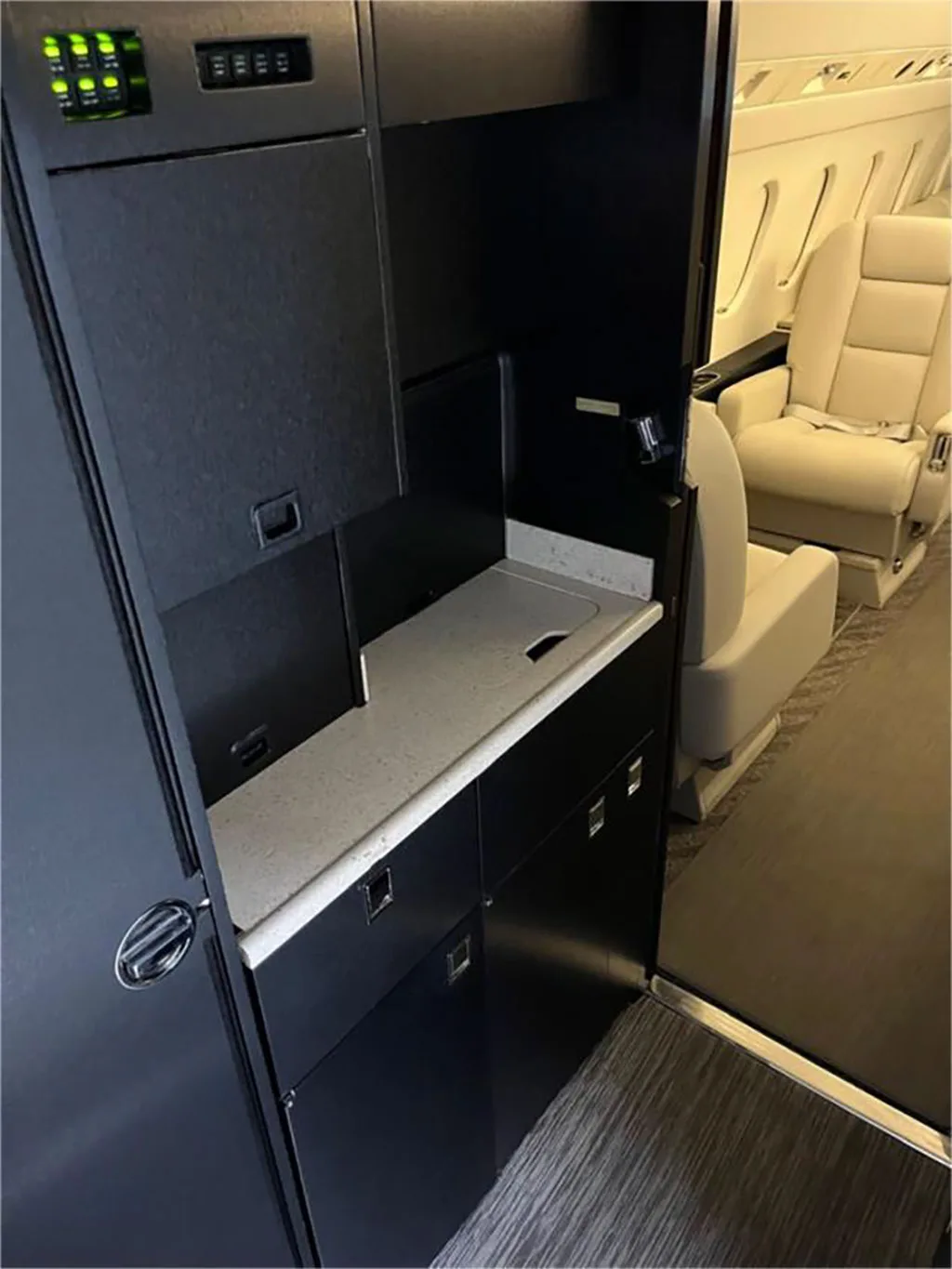 The aircraft's galley area with a light countertop, sink, and dark wood cabinetry, looking towards the passenger cabin.