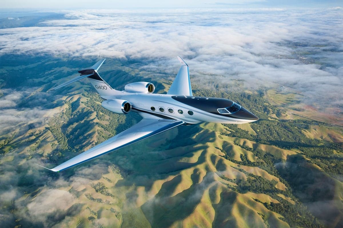 A Gulfstream G400 flying over a mountainous landscape with clouds.