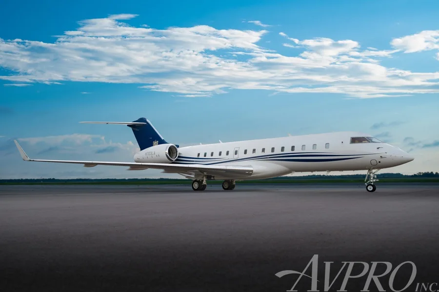 A Bombardier Global 6000 business jet with blue and white livery parked on a tarmac under a blue sky.
