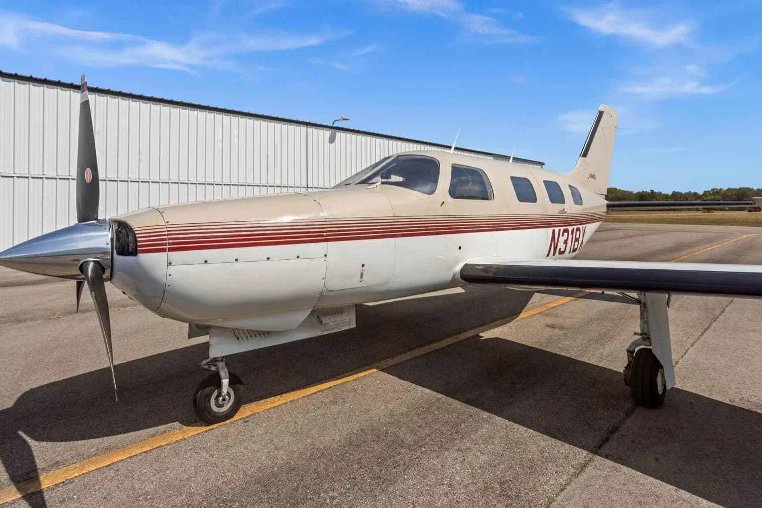 A front-side view of the Piper Malibu N31BX, showing the propeller and nose landing gear on the tarmac.