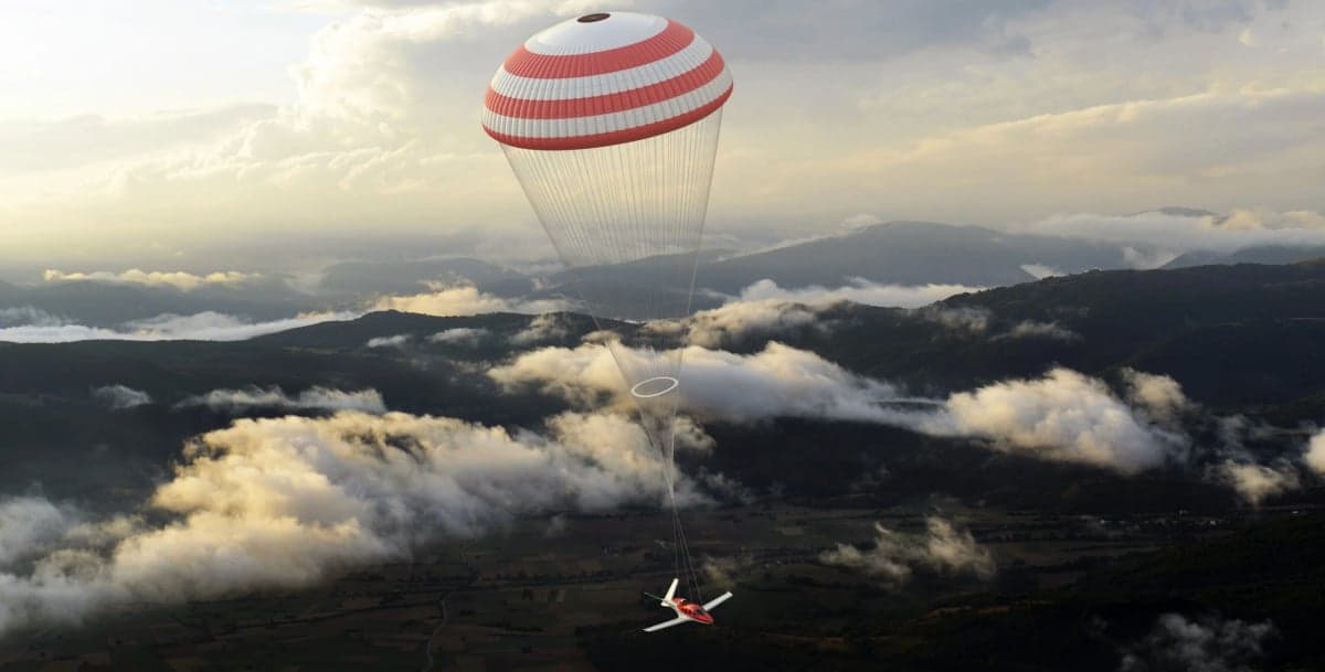 A Cirrus Vision Jet deploys its parachute system over a mountainous landscape.
