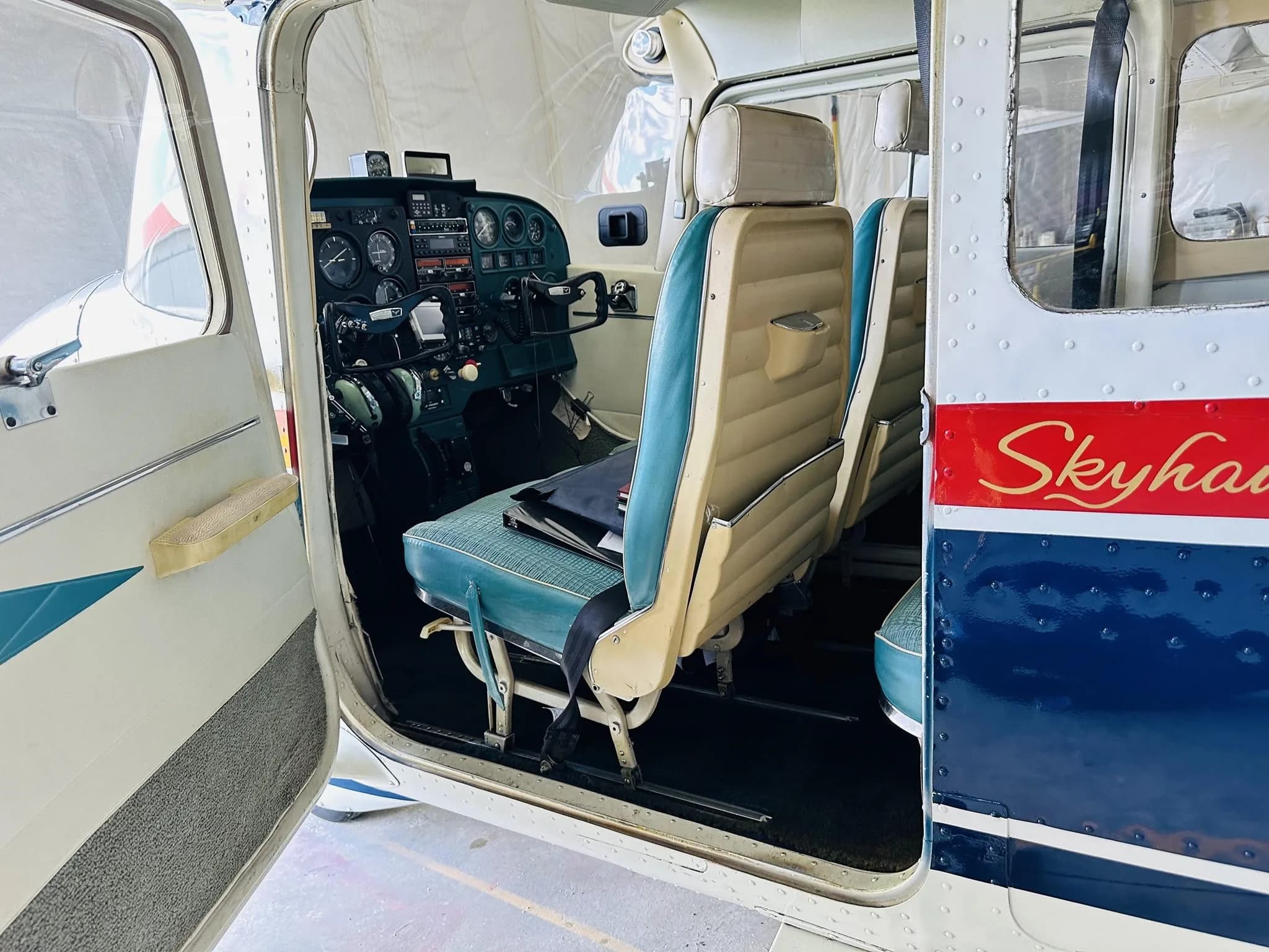 The interior of a Cessna Skyhawk showing blue and tan seats and the cockpit panel.
