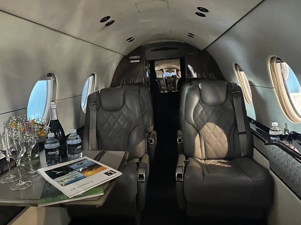 The aircraft's interior features leather seats, a table with champagne, and reading materials.