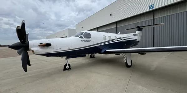 A head-on view of a white and blue Pilatus PC-12 turboprop aircraft with its propeller blades spread.