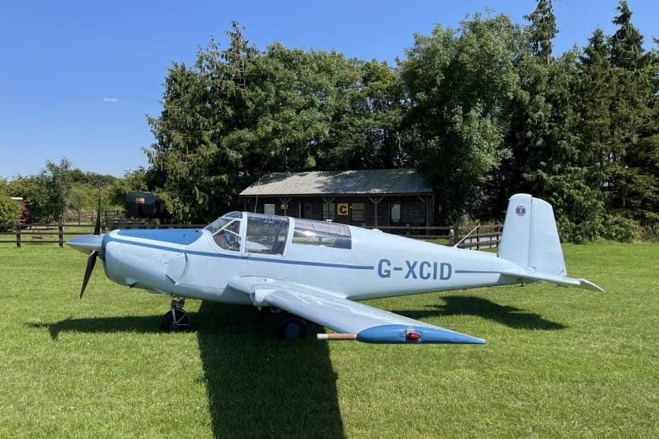 Side view of a light blue aircraft on a grassy field.