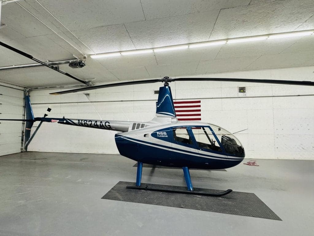 A Robinson R66 helicopter with a blue and silver paint scheme inside a hangar.