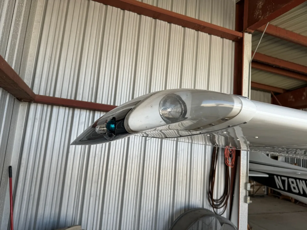 A close-up view of the wingtip of a white aircraft with navigation lights, inside a hangar.