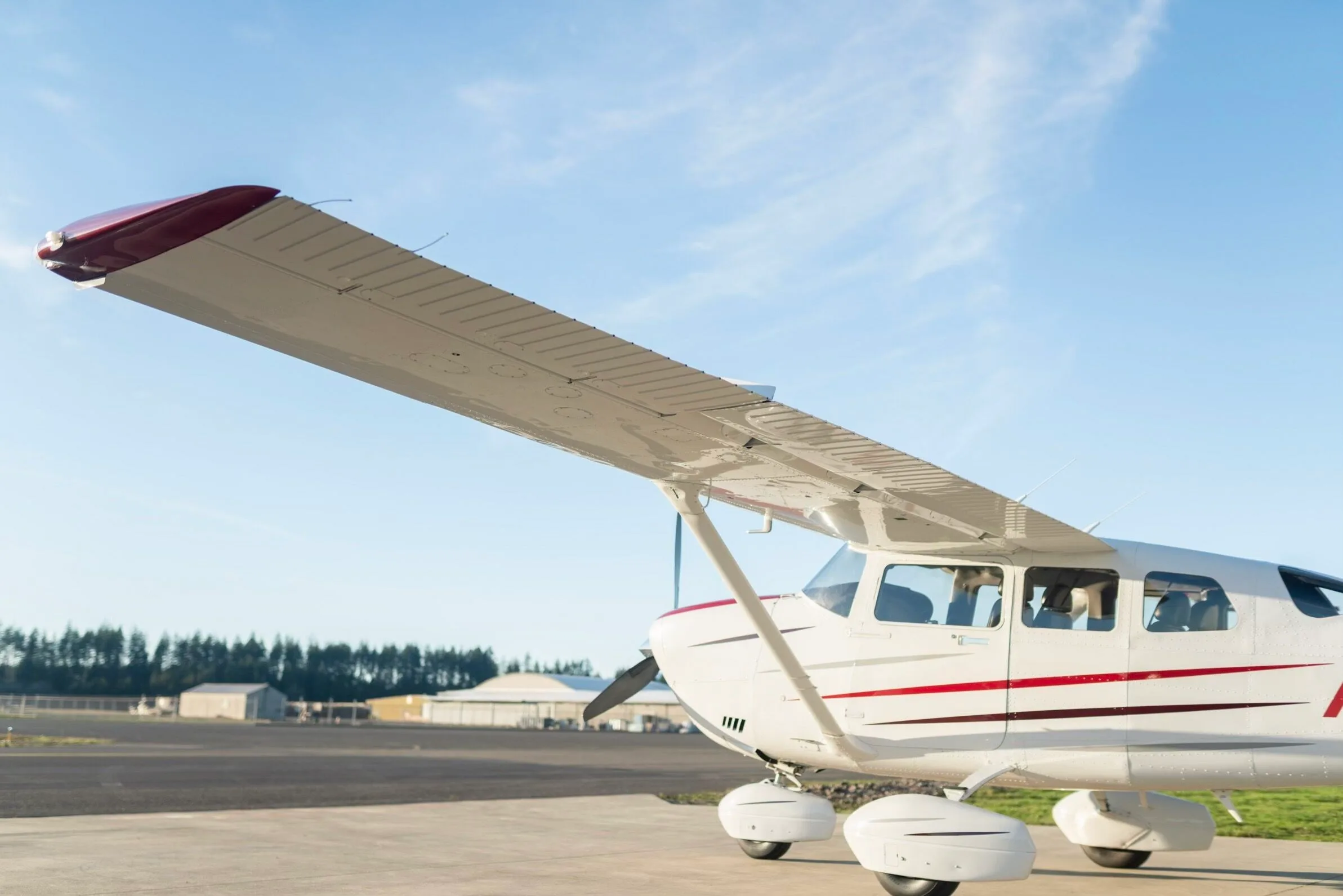 A close-up view of the front fuselage and wing of a white Cessna aircraft with red stripes, parked on a tarmac.