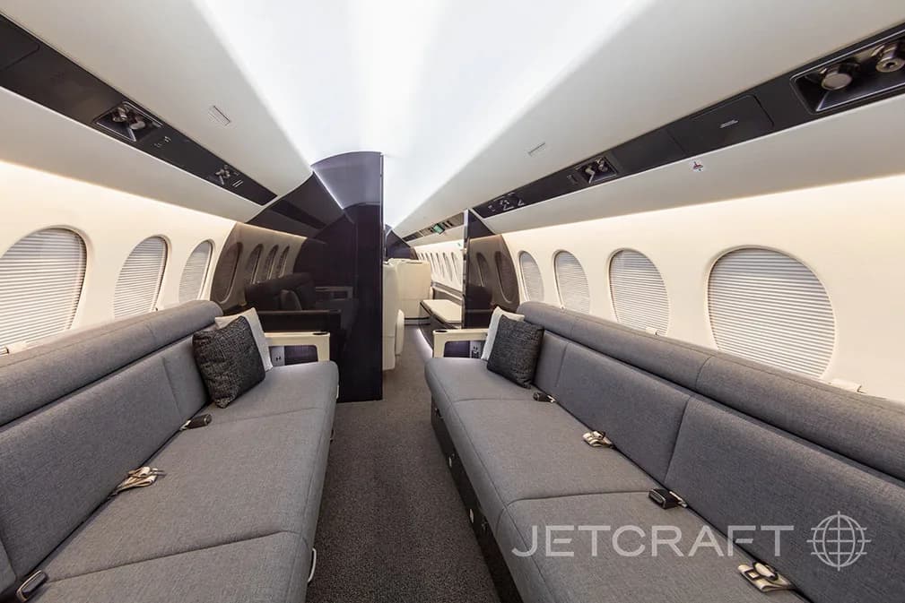 A private jet cabin featuring two long grey fabric sofas facing each other, with dark accent pillows.