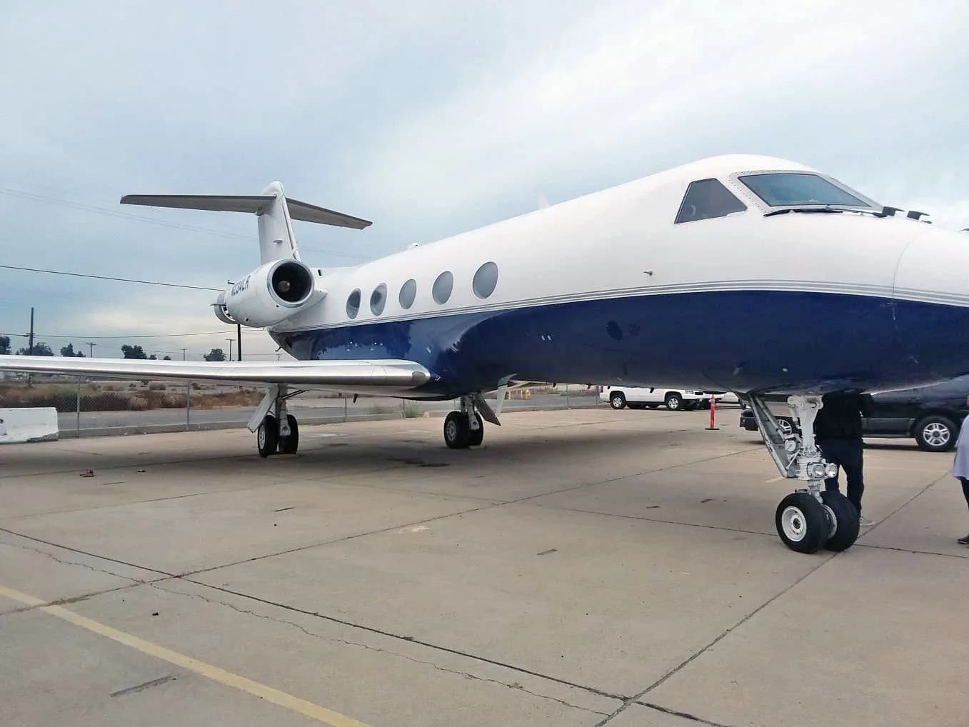 A Gulfstream G-IV business jet, registration N234LR, in a white and dark blue paint scheme, parked on a tarmac with a cloudy sky.
