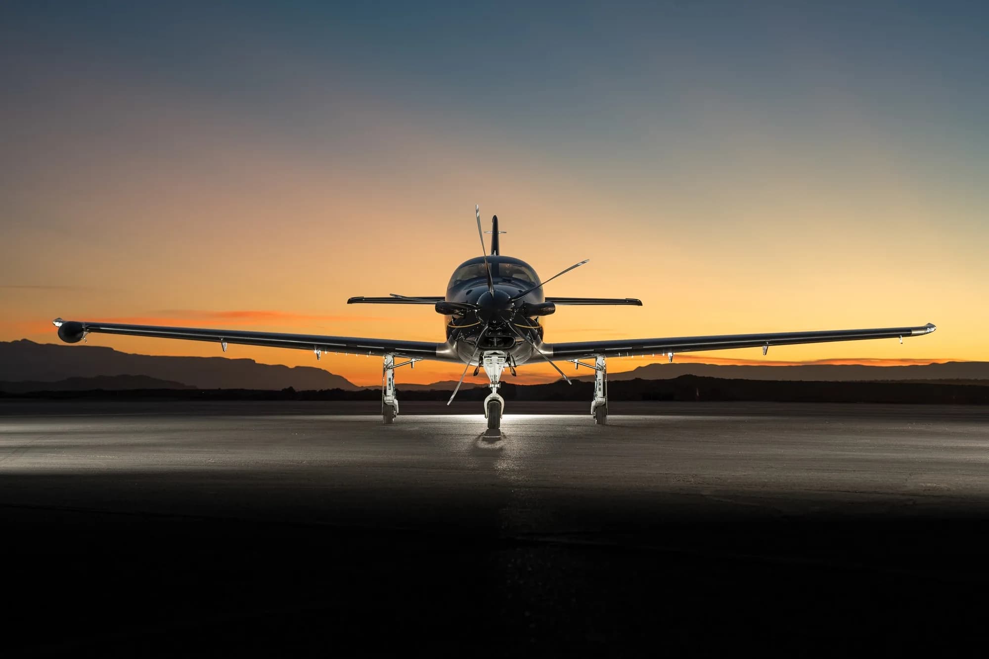 A black and gold Epic E1000 GX aircraft is viewed from the front, parked on a tarmac at sunset.