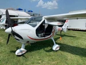 A white Bristell aircraft with red accents parked on a grassy field.