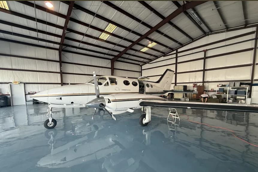 A white Cessna 414 aircraft with gold and black stripes, parked in a hangar, viewed from the front-left side.