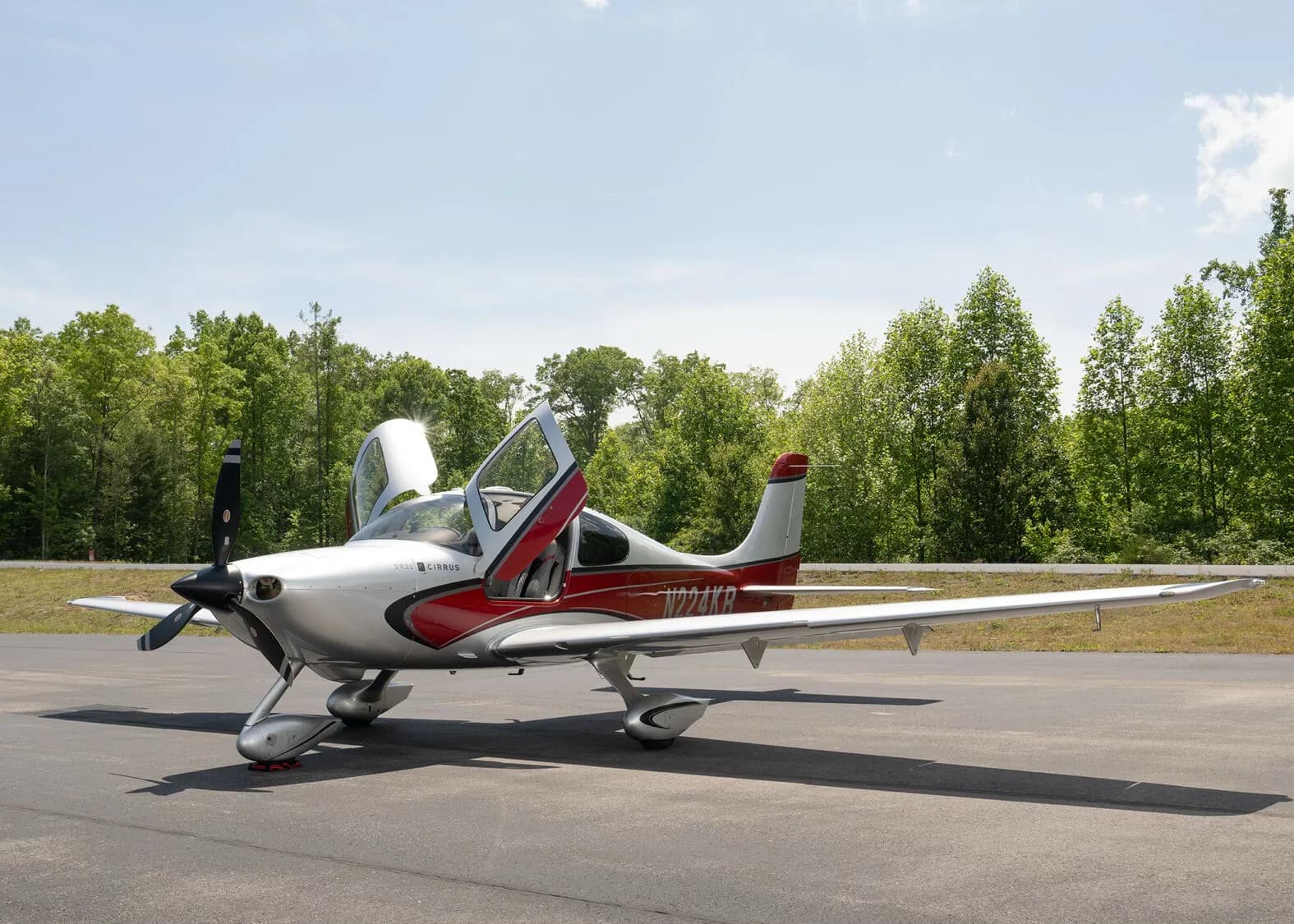 A silver and red Cirrus SR22 aircraft, N224KR, with both gull-wing doors open, parked on an asphalt ramp.