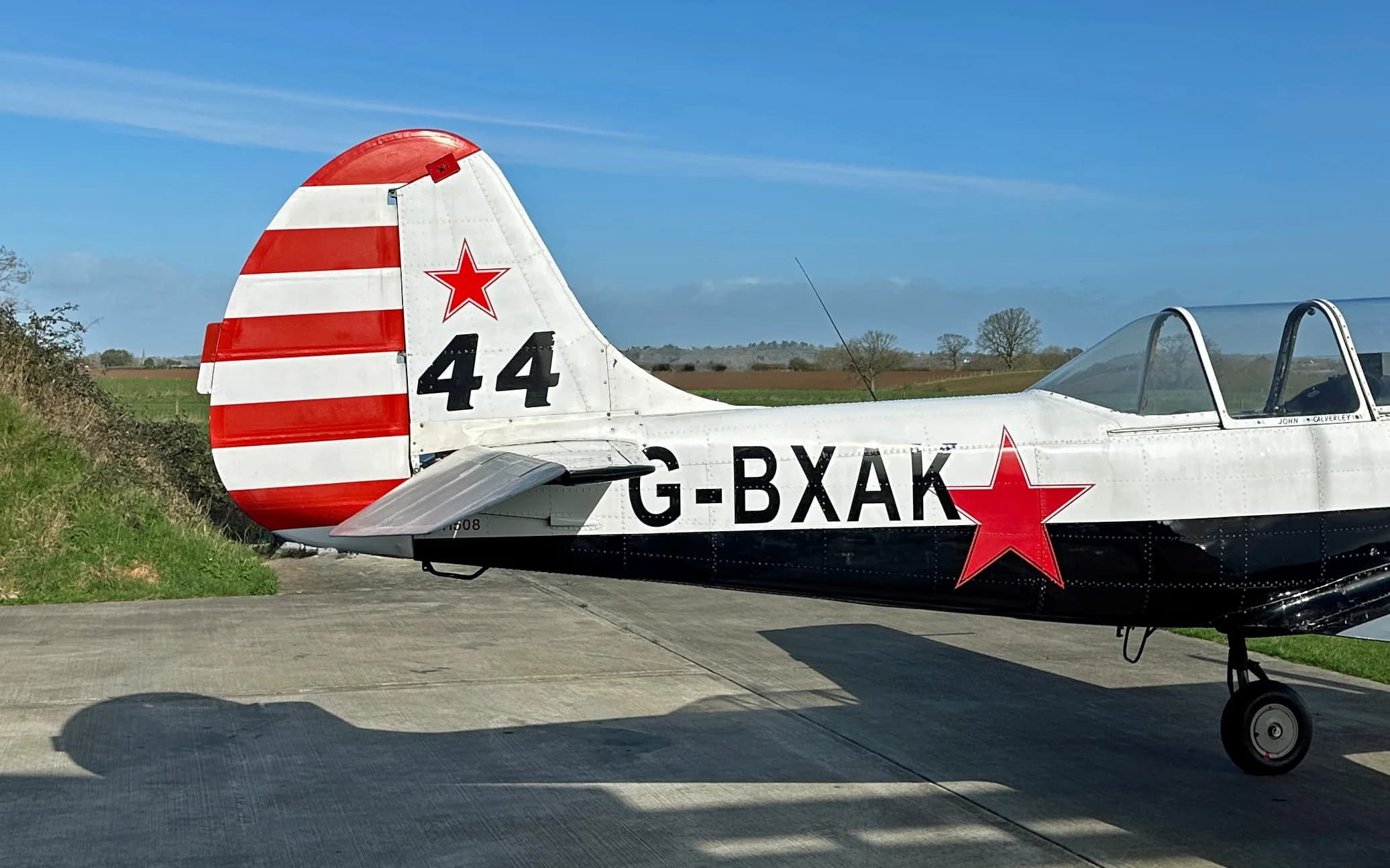 A close-up side view of the tail and rear fuselage of a Yak-52 aircraft, showing the red and white striped tail and a red star.