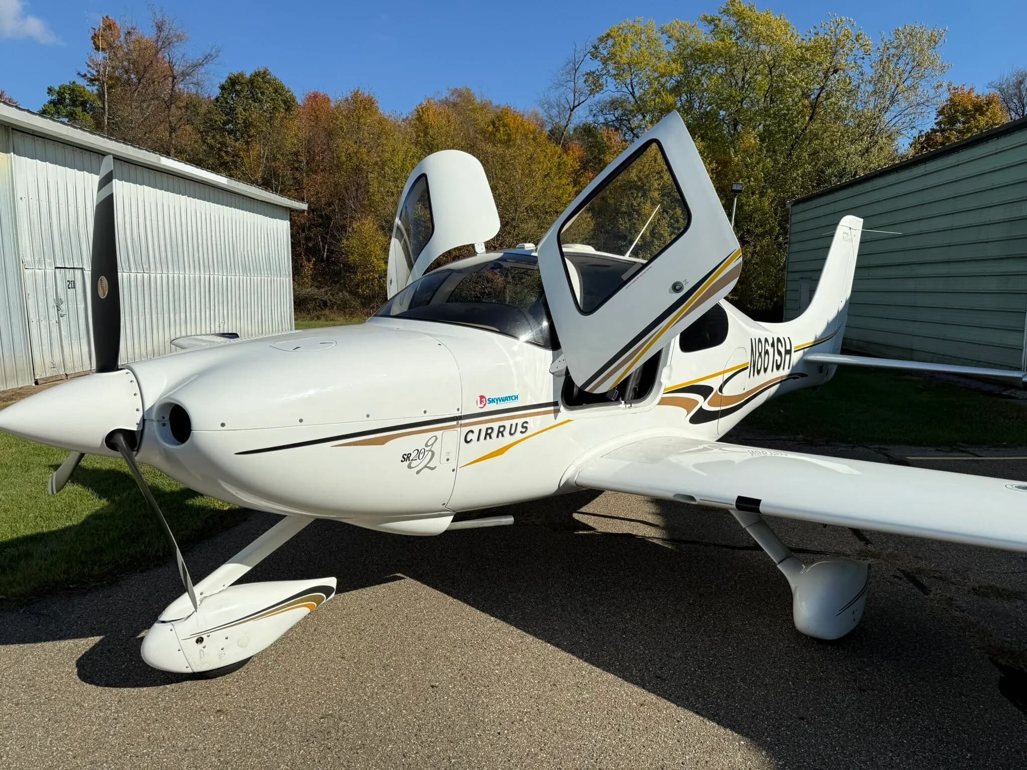 A front-side view of a white Cirrus SR20 aircraft, registration N861SH, with both gull-wing doors open, parked on an asphalt ramp.