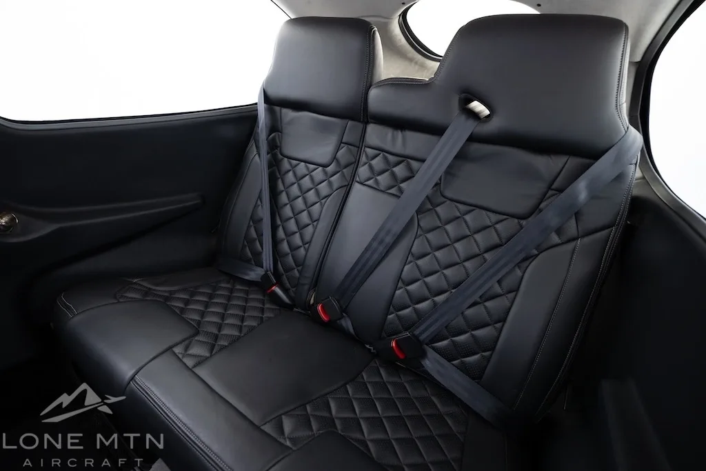 A close-up view of the black leather rear seats of an aircraft cabin with diamond stitching.