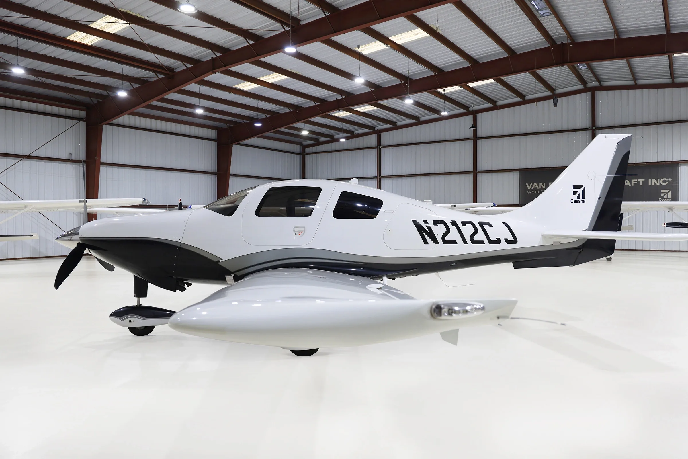 A white and black Cessna TTx aircraft (N212CJ) is parked in a hangar, viewed from the side.