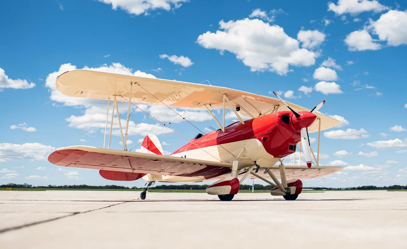 A red and white biplane sits on the tarmac under a blue sky with fluffy clouds.