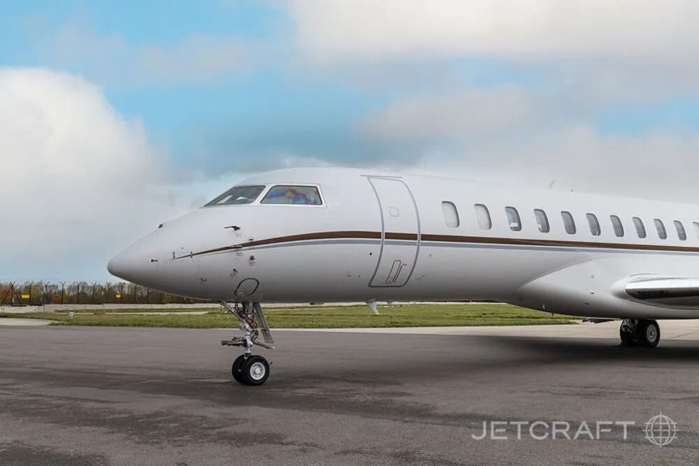 A close-up side view of the nose and front fuselage of a white Bombardier Global business jet on an airfield.