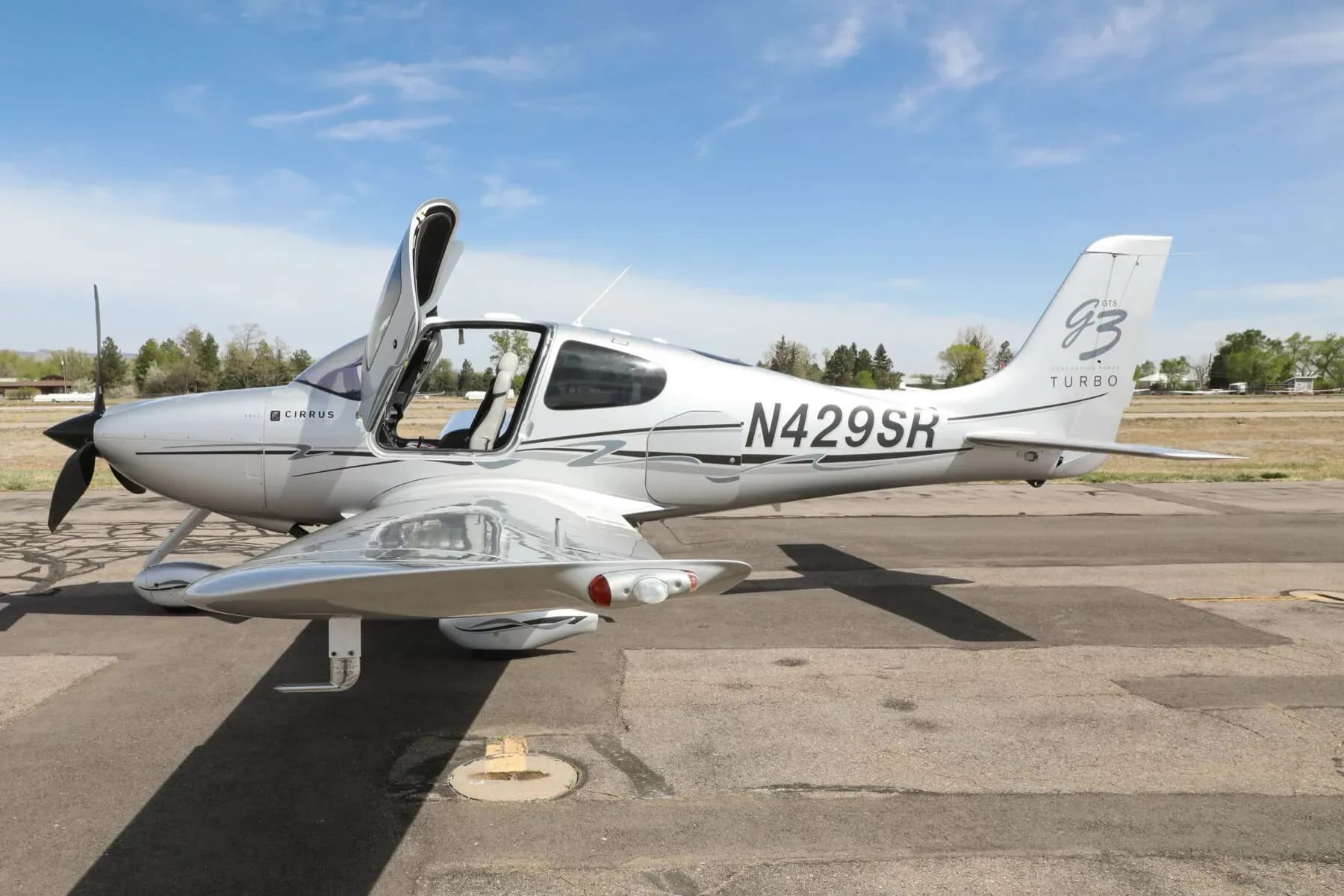 A silver Cirrus SR22T aircraft with black and grey accents, registration N429SR, with its door open, parked on an asphalt ramp.