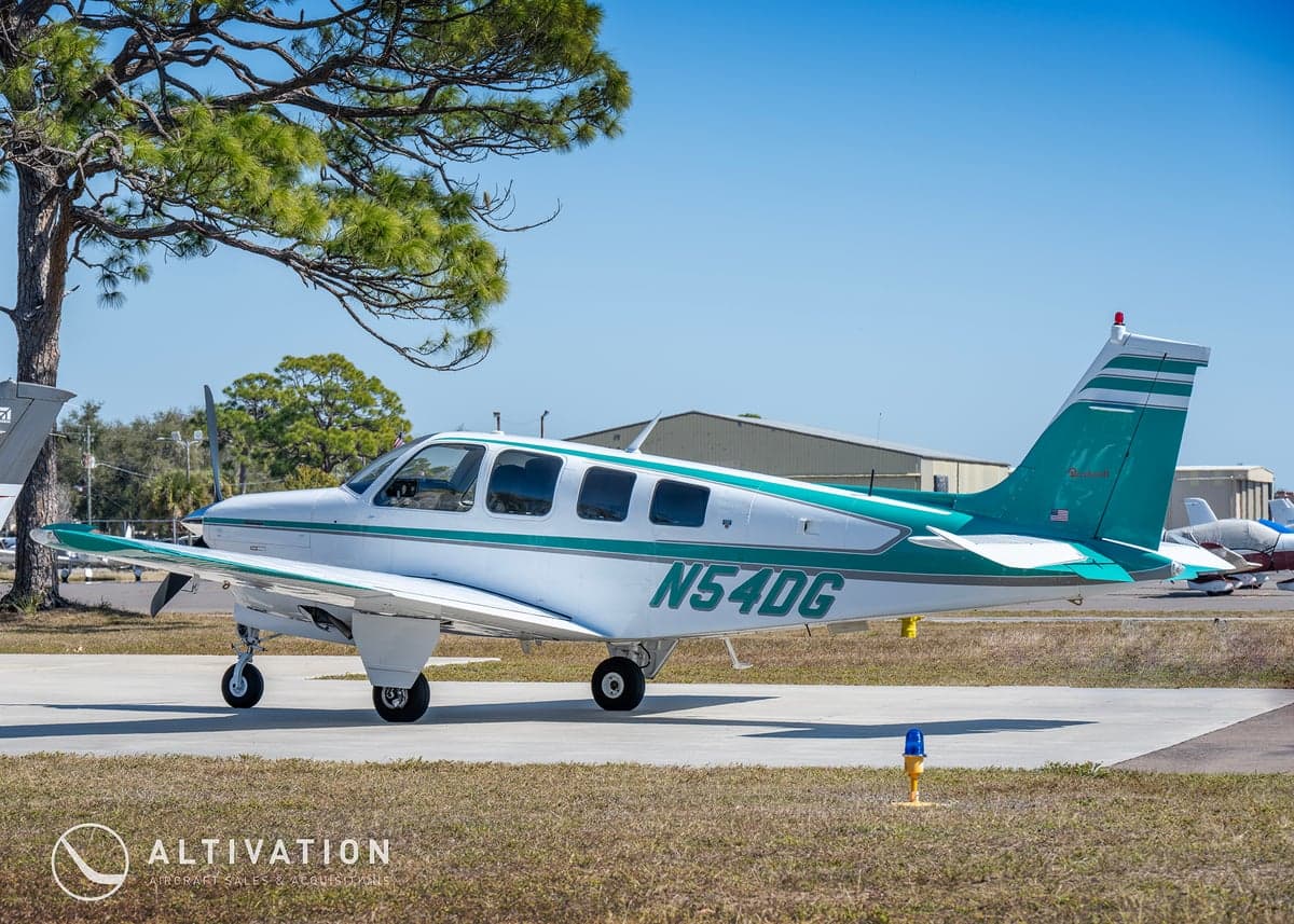 A Beechcraft Bonanza with a white and green paint scheme on the tarmac.