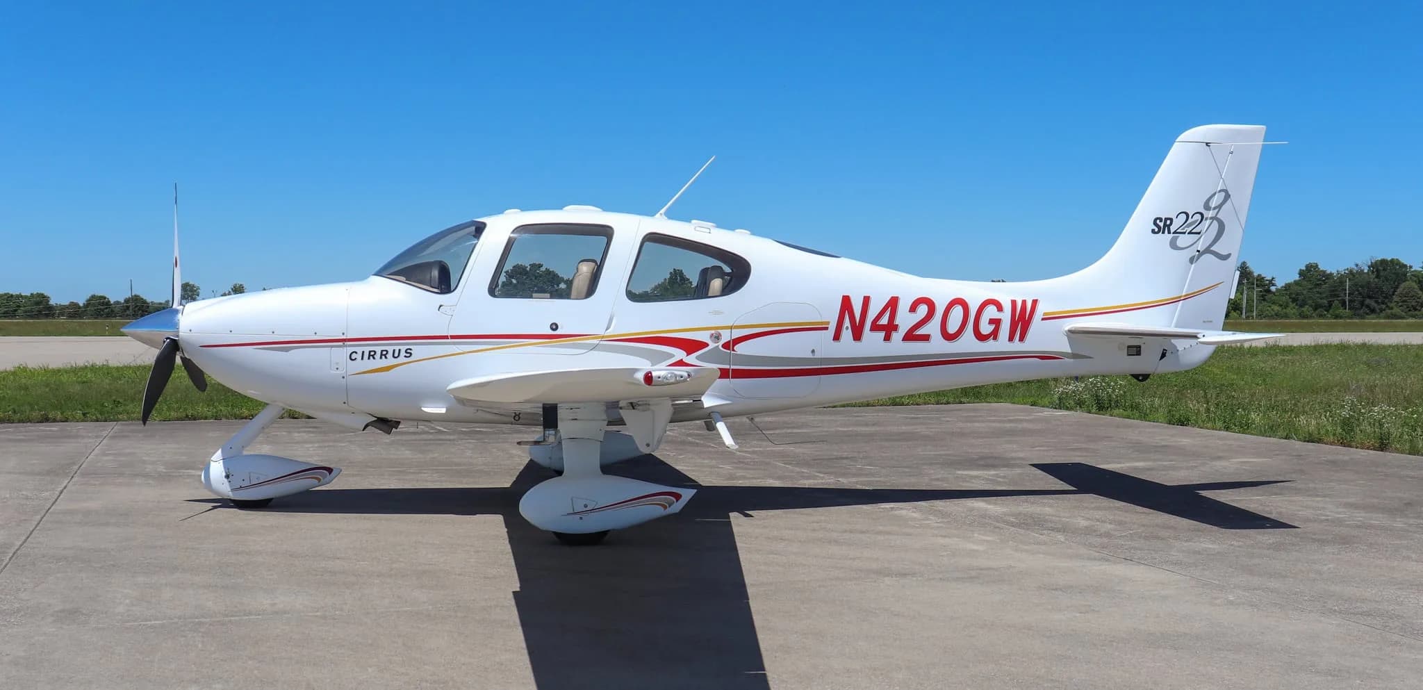 Side view of a white Cirrus SR22 aircraft with red and gold stripes on a tarmac.