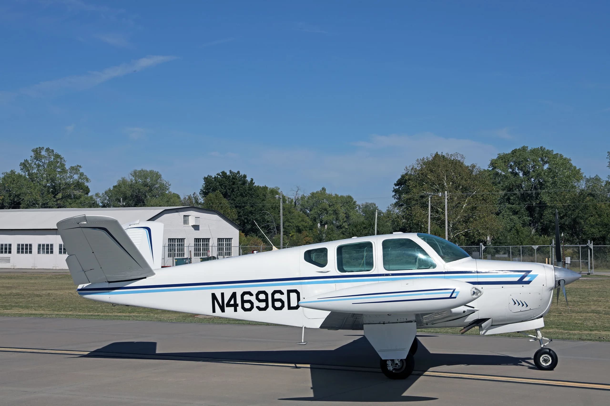 A side view of the white single-engine aircraft N4696D with blue stripes, parked on an airfield.