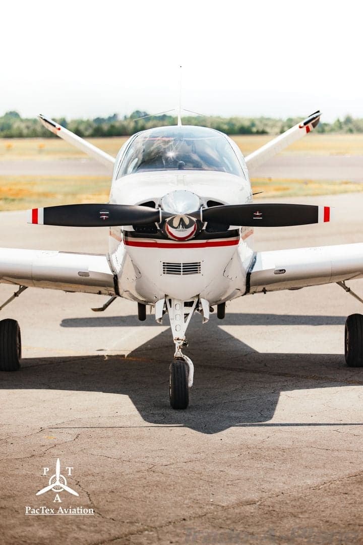 Close-up frontal view of a white single-engine aircraft showing the propeller and nose.