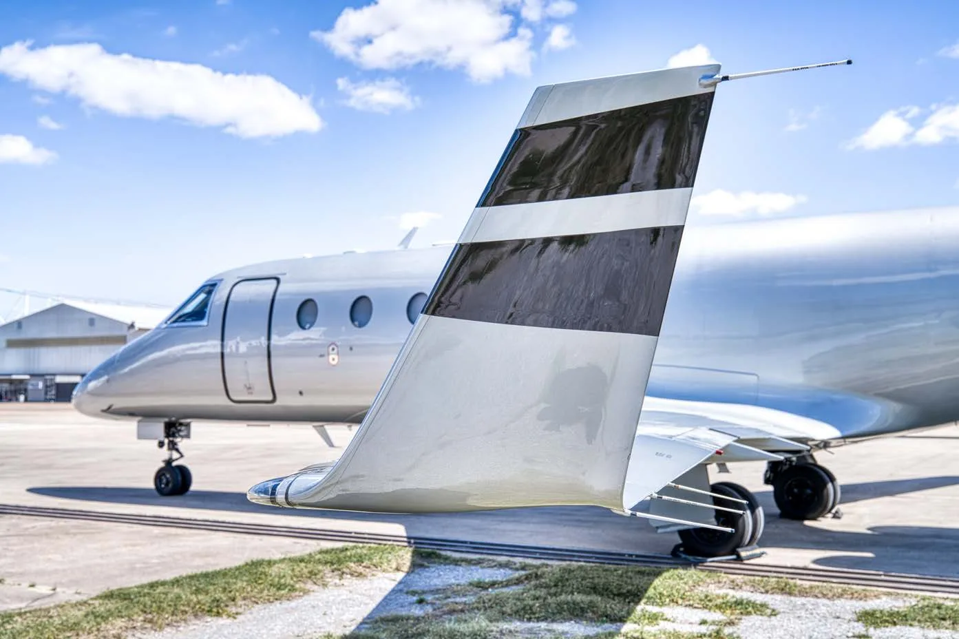 A close-up view of the silver tail of a business jet with black stripes.
