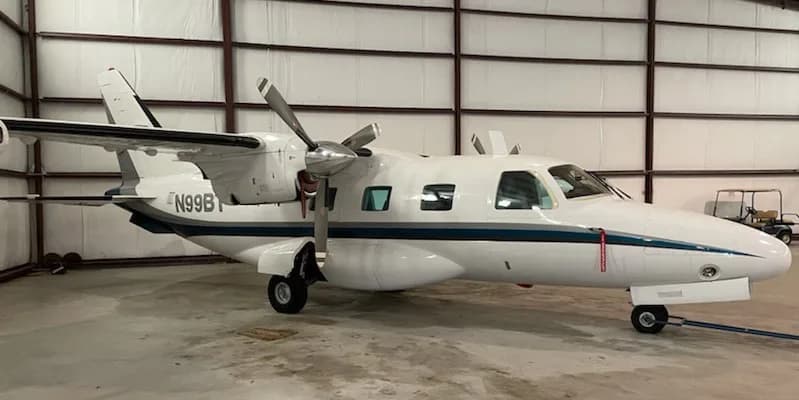 A white twin-engine turboprop aircraft with a blue stripe, registration N99B, parked inside a hangar.