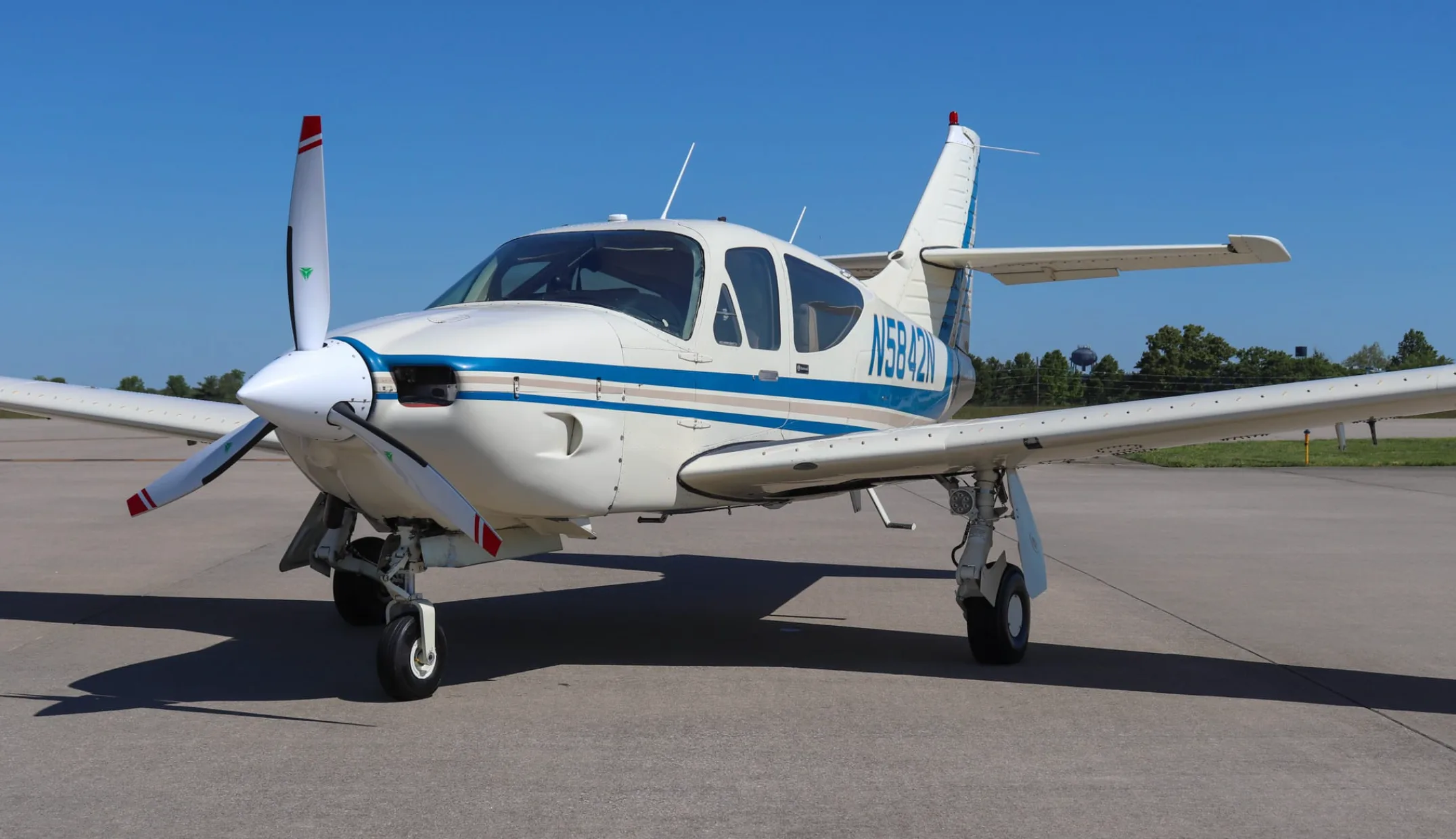 Front-left view of a white single-engine propeller aircraft with blue and tan stripes, registration N5842N, parked on an airfield.