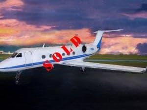 A white jet aircraft with blue stripes parked on the tarmac, marked with a 'SOLD' overlay.