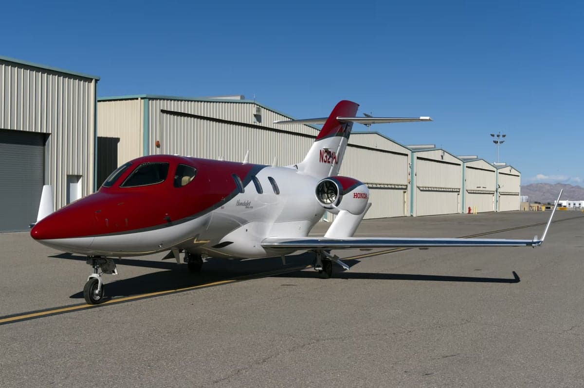 Side view of a red and silver HondaJet with tail number N321HJ parked on the tarmac.