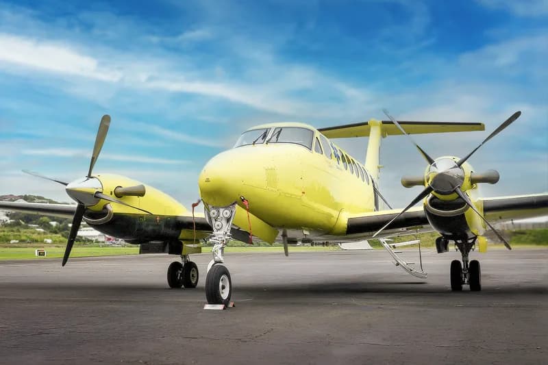 A bright yellow and black twin-engine turboprop aircraft, likely a Beechcraft King Air, parked on an asphalt runway under a blue sky.
