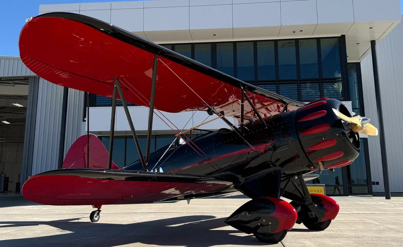 A black and red biplane is parked in front of a modern building with large windows.