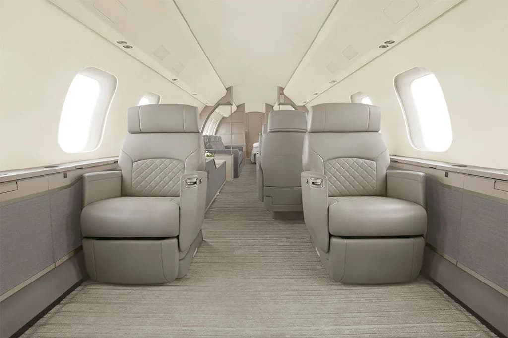 A luxurious aircraft cabin interior with light grey quilted leather seats and a light-colored carpet.