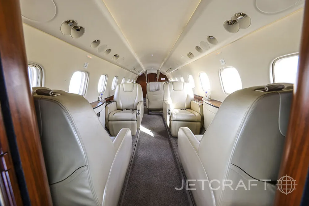 The interior cabin of a private jet featuring light beige leather seats arranged in a club configuration.