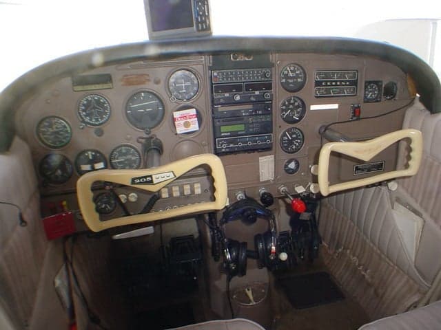 The cockpit of a Cessna 206 aircraft, showing the instrument panel, dual yokes, and avionics.